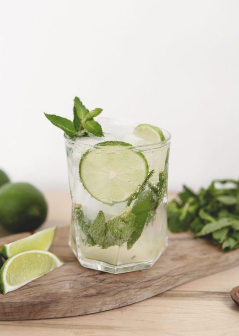 mojito mocktail in glass on wood cutting board with lime and mint around it