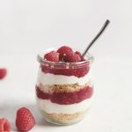 glass jar filled with layers of crust, cheesecake filling raspberry filling