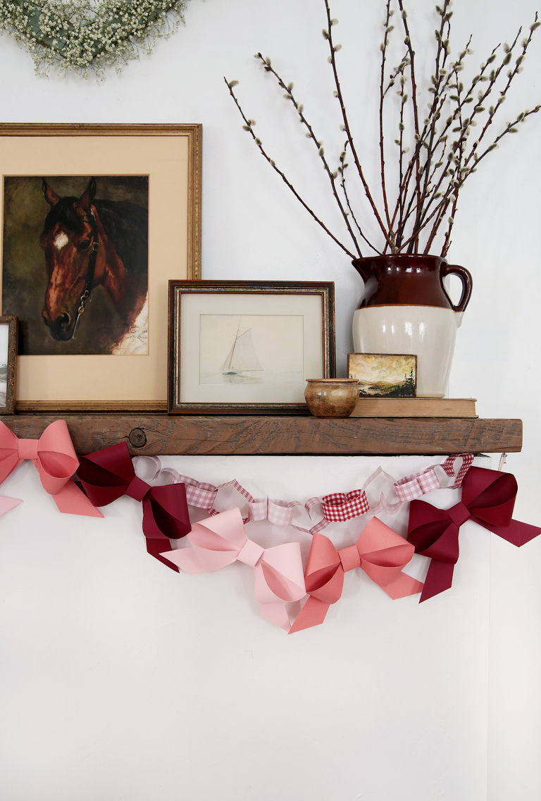 paper bow garland hanging from wood mantel with vintage paintings on mantel
