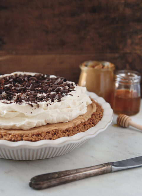 side view of pie in white fluted pie plate with whipped cream on top of pie and chocolate shavings on top