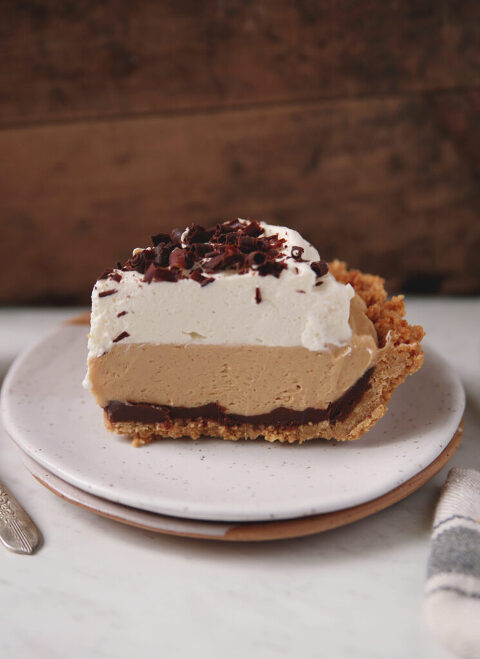 side view of slice of pie with nutter butter crust, layer of chocolate ganache, creamy peanut butter filling, topped with whipped cream and chocolate shavings