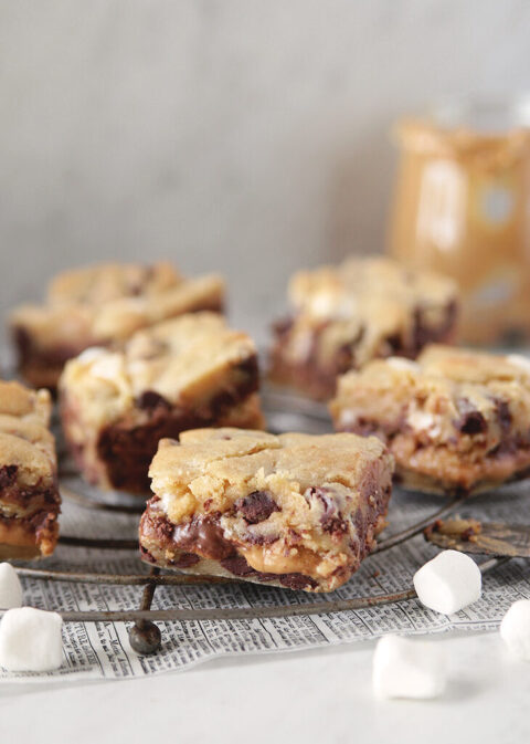 close up side view of cut s'mores cookie bars with peanut butter sitting on cooling rack with mini marshmallows around it