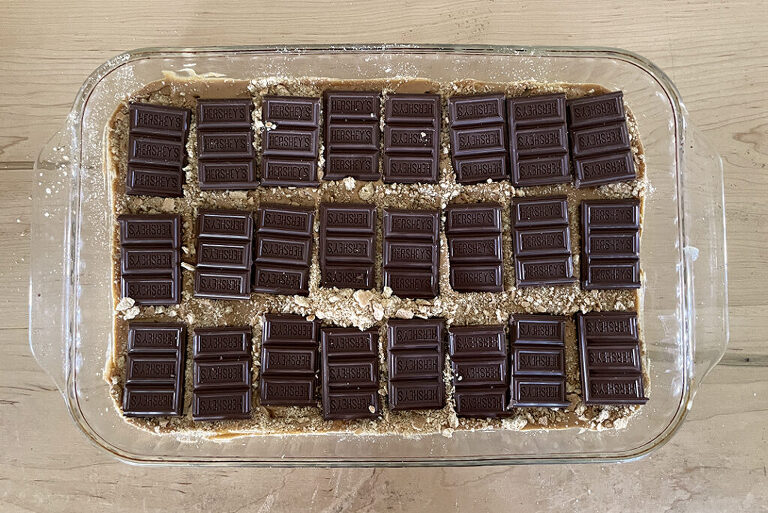 glass pan with crushed graham crackers in it with broken up hershey bars on top