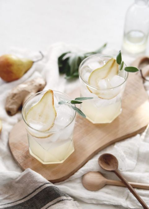 two glasses on cutting board with pear and sage in drinks