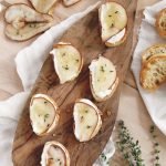 pear and whipped goat cheese crostini appetizers on cutting board next to fresh thyme