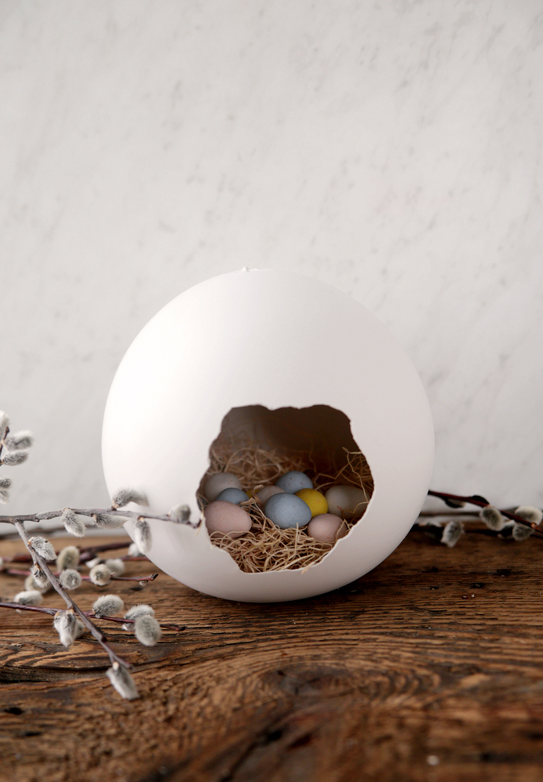 giant balloon plaster egg with hole in the side filled with easter grass and cadbury mini eggs with pussy willow branches around it