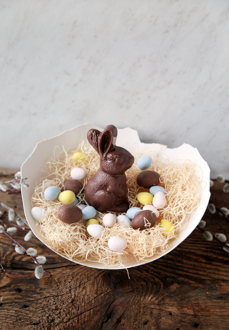 large plaster egg filled with easter grass and easter candy sitting on wood board