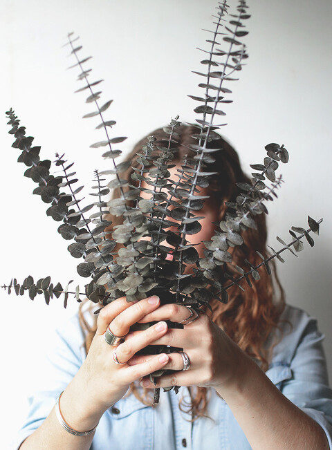 woman holding branches of dried eucalyptus in front of her face