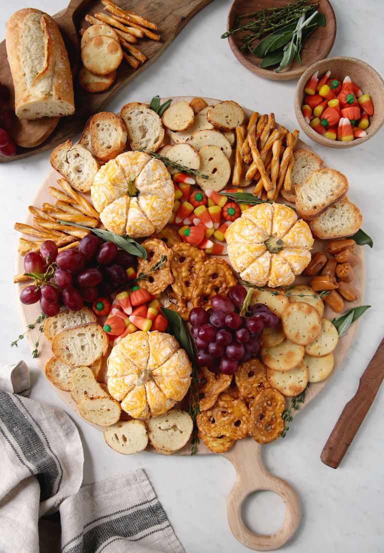 top view of fall charcuterie board with cheese balls, crackers, candy corn, caramels, grapes and crostini on it