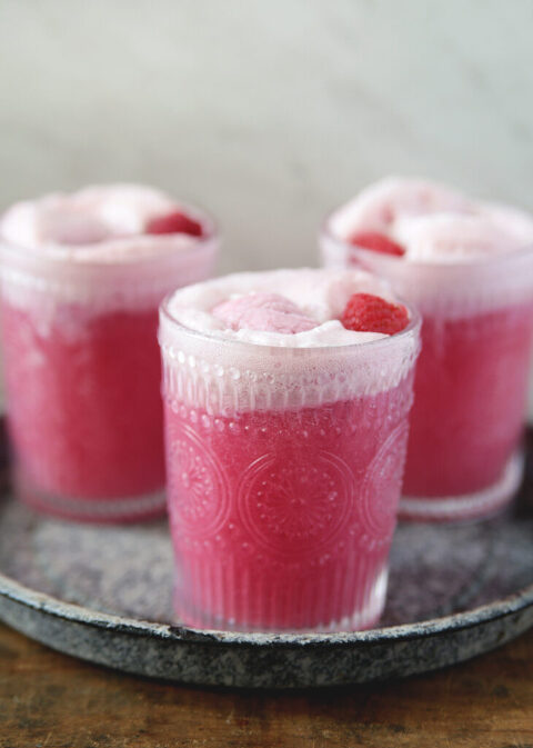 3 glasses of raspberry sherbet party punch with raspberry sherbet and raspberry floating in top of glasses