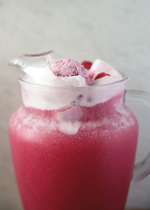 glass pitcher of pink raspberry punch with raspberry sherbet and raspberries on top