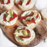 red pepper artichoke pesto crostini on wood cutting board