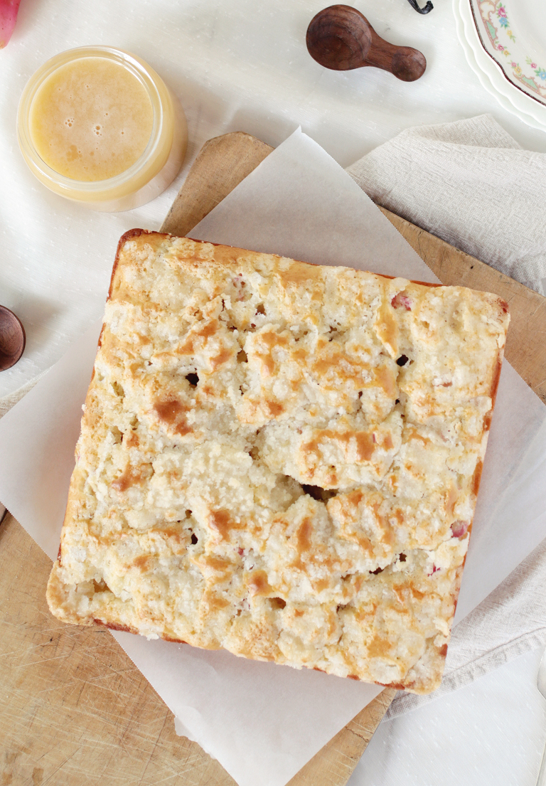 square rhubarb cake on wood cutting board with jar of vanilla sauce next to cake