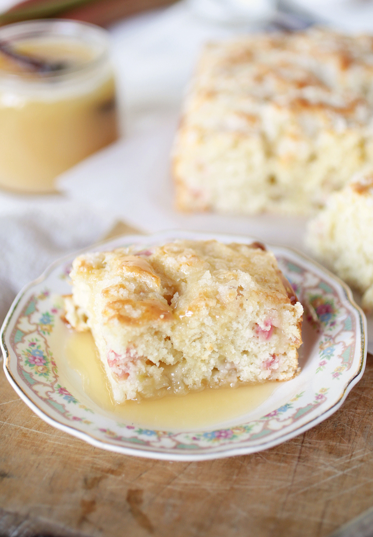 square slice of rhubarb cake on floral plate with vanilla sauce over cake