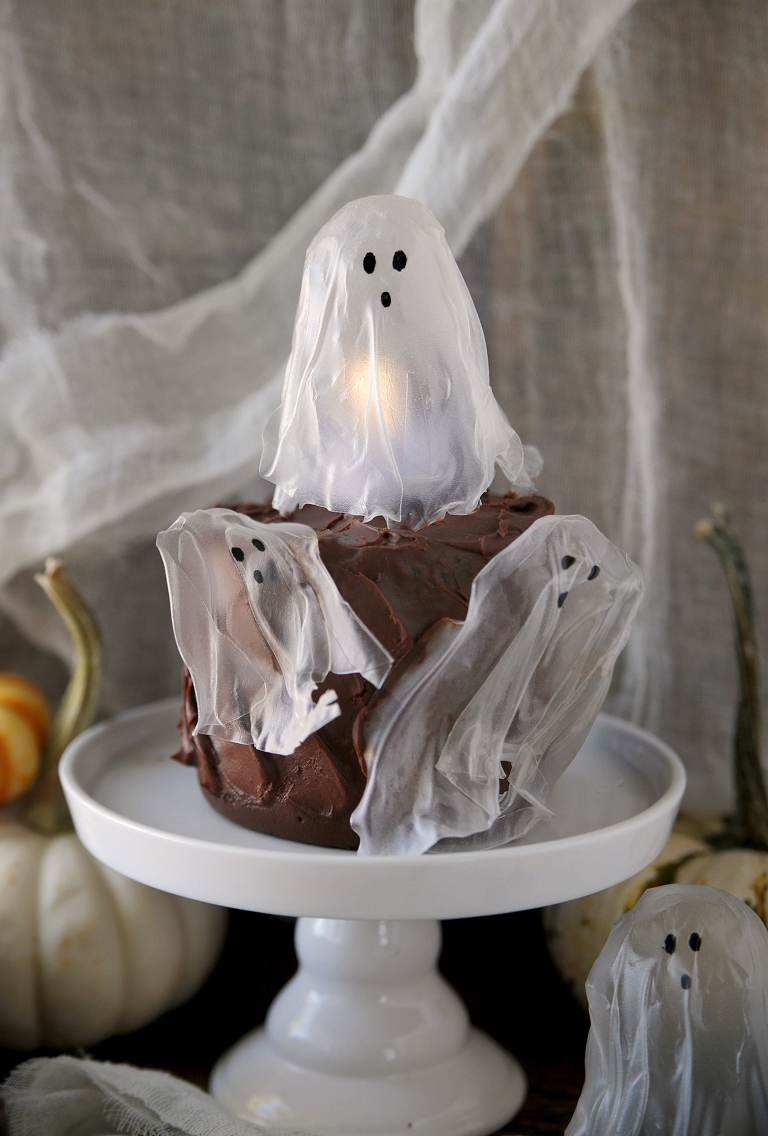 three rice paper ghosts stuck on chocolate cake with a tea light under the ghost on top of cake