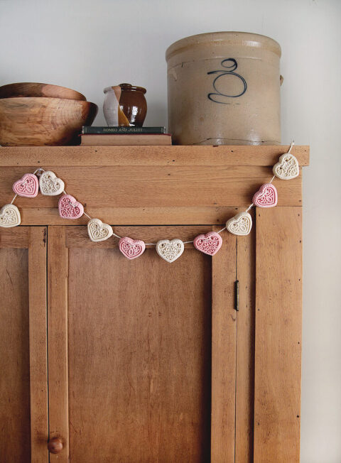 pink and white heart garland hanging on antique wood cabinet with books and antiques on top of cabinet
