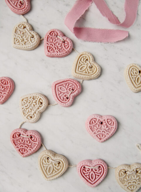 pink and white salt dough hearts on twine laying on a marble board with pink ribbon next to it