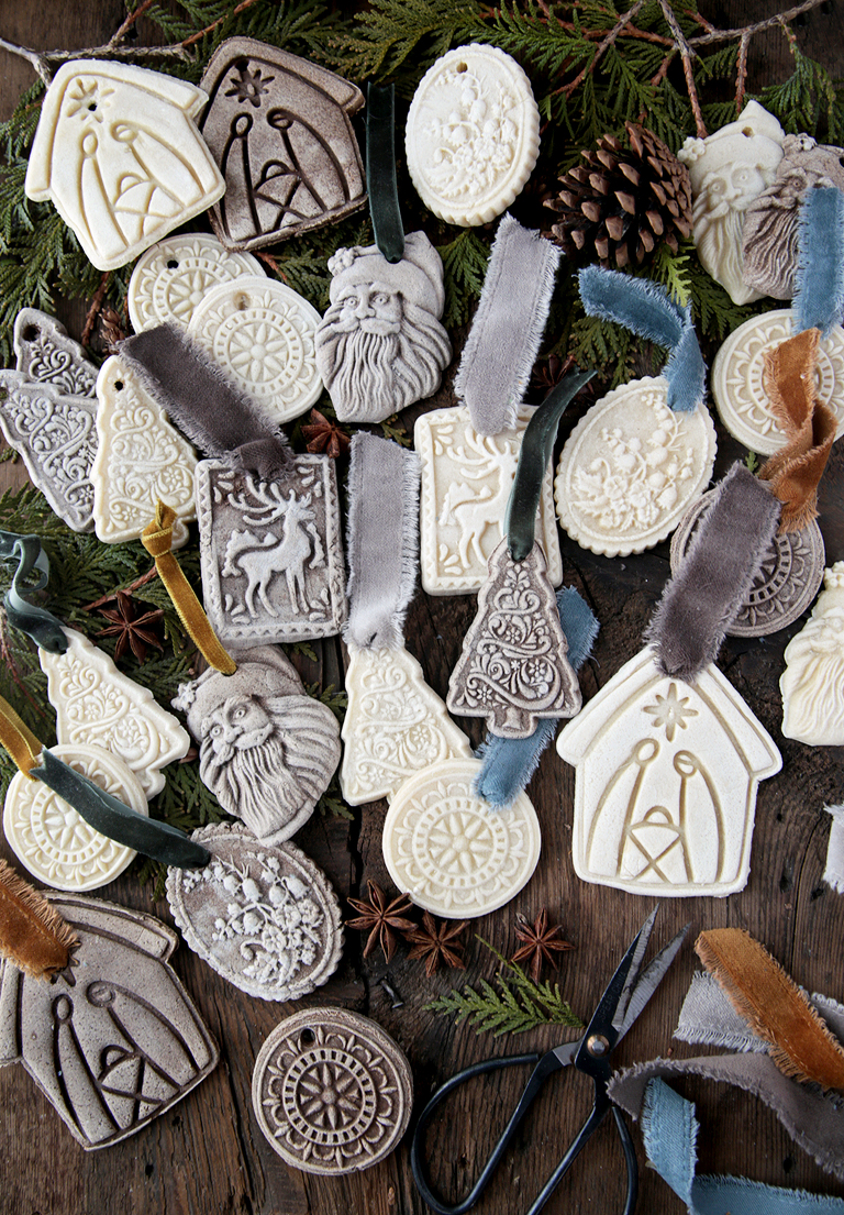 various salt dough christmas ornaments laying on wood board with greenery, ribbon, pinecone and anise laying with them