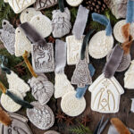 various salt dough christmas ornaments laying on wood board with greenery, ribbon, pinecone and anise laying with them