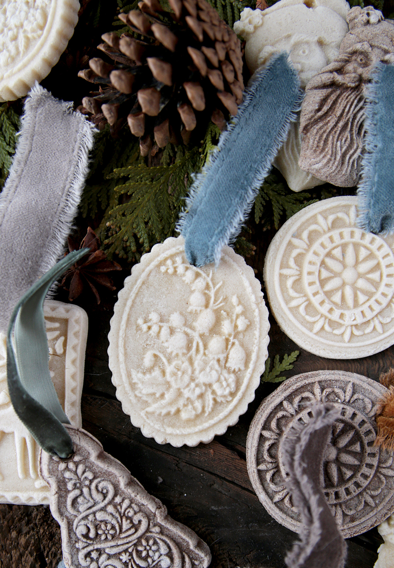 white and gingerbread salt dough ornaments laying on wood board with greenery and pinecone