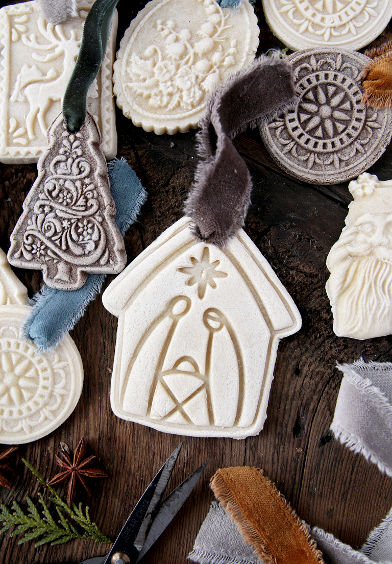 nativity scene salt dough ornament with ribbon laying next to christmas salt dough ornaments on wood board