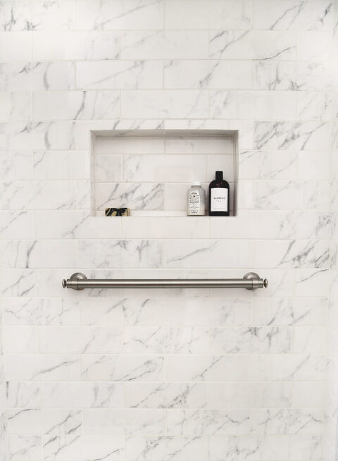 horizontal brushed nickel shower grab bar installed on marble tile shower wall under built in shower niche with shampoo bottle in it