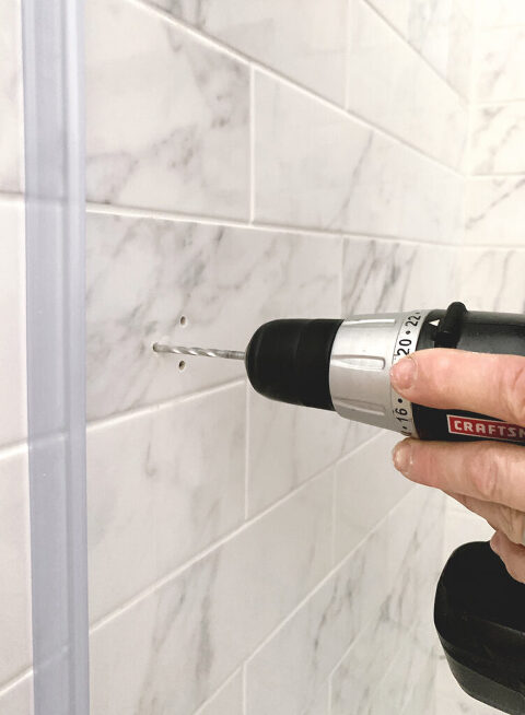 a drill with masonry drill bit drilling into tile shower wall