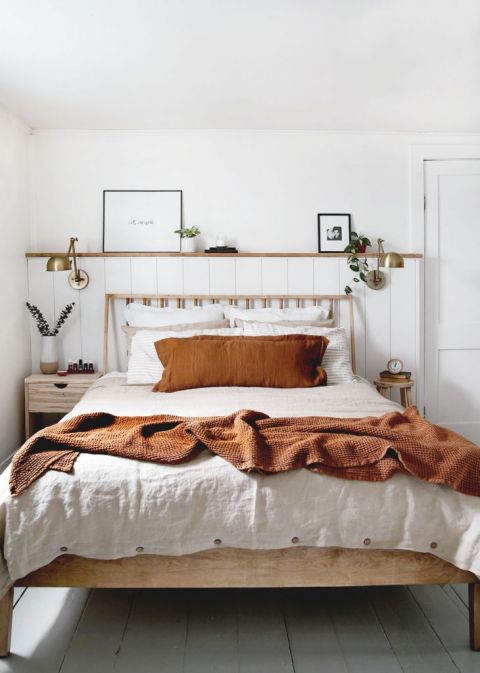 wood bedframe with linen blankets on it brass lamps on wall