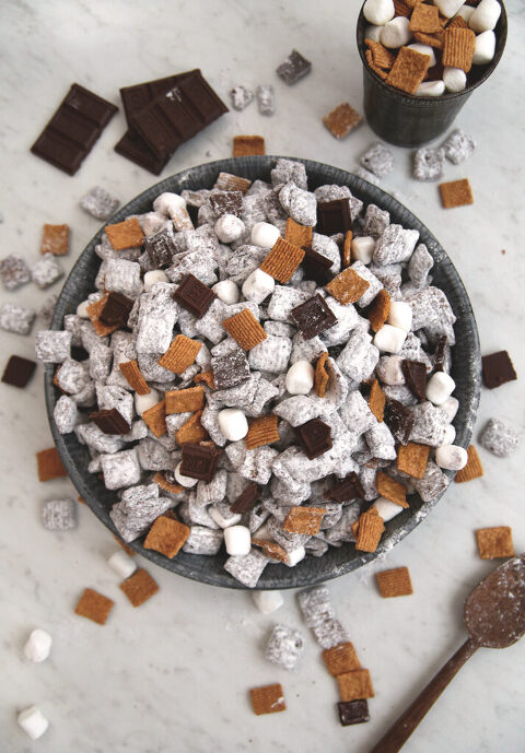 vintage metal pan filled with s'mores puppy snack mix next to wooden spoon and metal measuring cup filled with golden graham cereal marshmallows