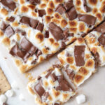 s'mores bars with one end cut into square pieces with chocolate bars and mini marshmallows around it