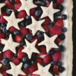 close up of lemon berry tart with fresh fruit on it and topped with shortbread cookie stars