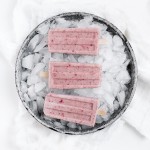 metal pie plate filled with ice with strawberry banana popsicles on the ice