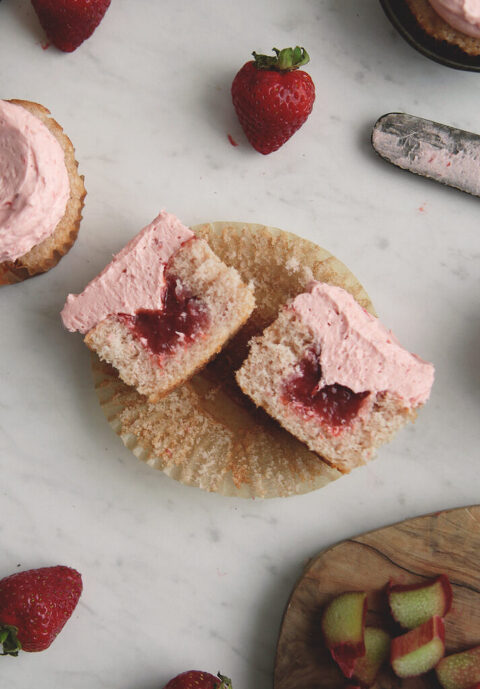 cut unshut cupcake with strawberry frosting on it and filled with strawberry rhubarb compote filling inside