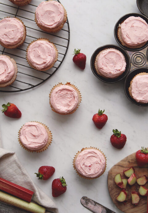 overhead shot of frosted strawberry rhubarb cupcakes with strawberries laying by cupcakes