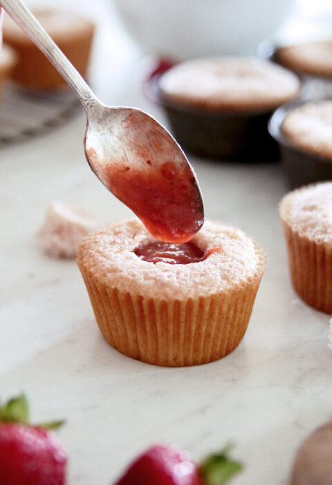 strawberry cupcakes with part-way cut out and a filling stuff spooned into hole
