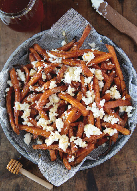 plate filled with sweet potato fries with goat cheese and hot honey on fries with honey stick and jar of honey next to plate
