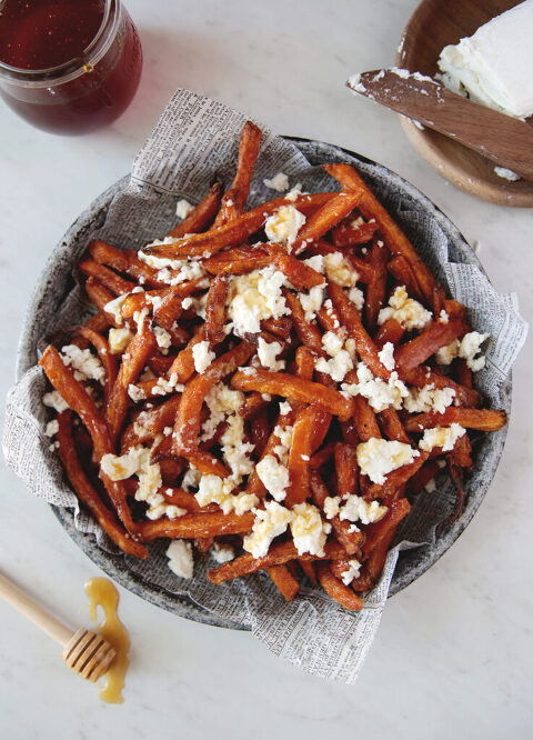 metal plate with sweet potato fries with goat cheese and hot honey on fries with honey stick and jar of honey next to plate