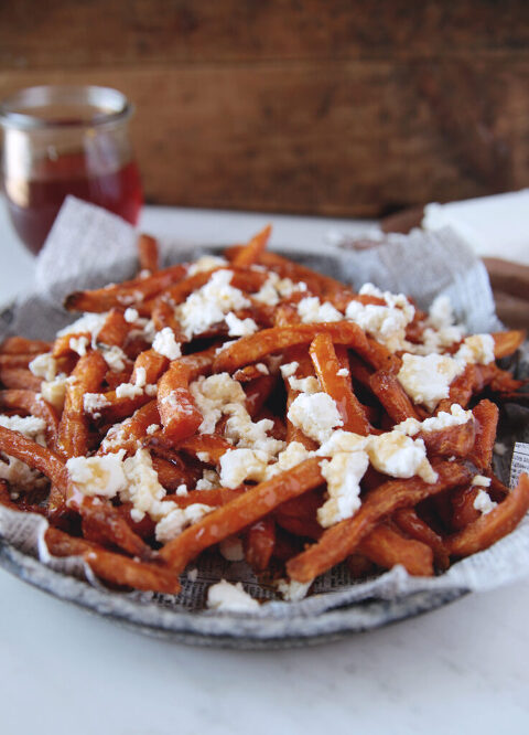 Plate of sweet potato fries with crumbled cheese and honey on fries, with jar of honey next to plate.