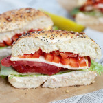 veggie bagel sandwich filled with peppers, cheese, tomatoes lettuce and cream cheese sitting on parchment paper
