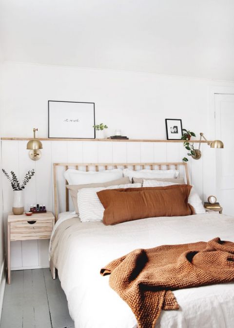 bed against white wall with wood shelf and brass lamps