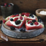 watermelon fruit pizza on metal plate with whipped cream cheese topping and mixed fruit on it