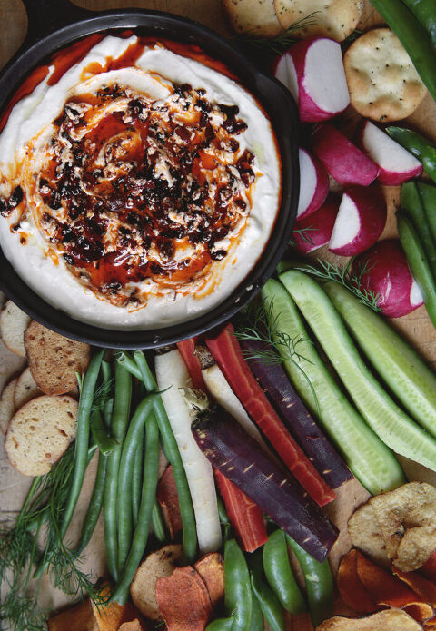 bowl of Cottage Cheese Chili Crisp Dip on cutting board with cut up vegetables and crackers surrounding it