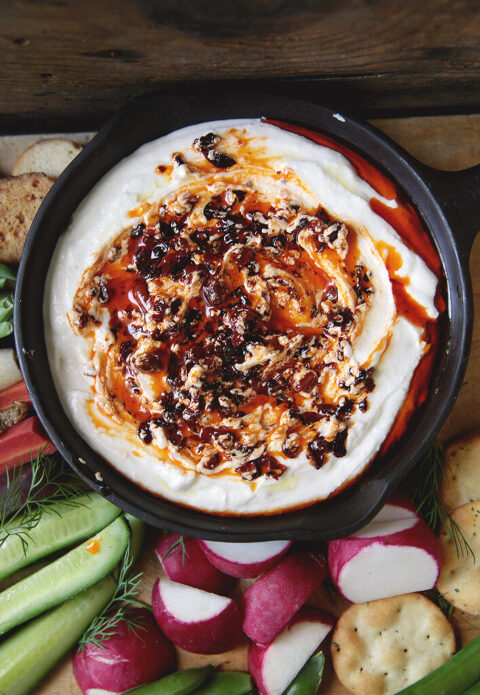 black bowl with cottage cheese chili crisp dip in it surrounded by cut up vegetables on wood cutting board