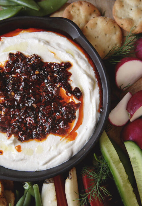 close up of bowl of whipped cottage cheese with chili crisp dip with veggies next to bowl