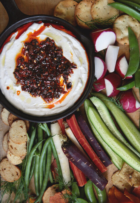 serving platter with bowl of whipped cottage cheese with chili crisp topping next to cut vegetables and crackers