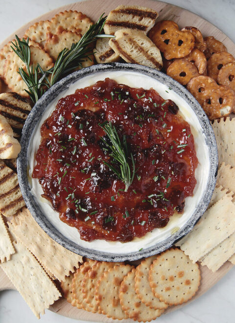 cutting board with crackers and crostini on it with whipped goat cheese fig rosemary appetizer in the middle