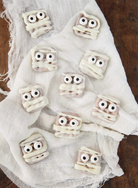 ten white chocolate dipped mummy pretzel bites on white cheesecloth background